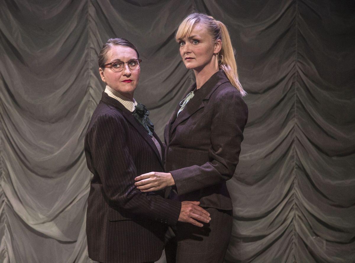 Scene fra The Einstein of Sex: to performere i jakkesæt står tæt sammen foran et gråt tæppe